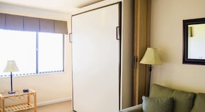 A room with a closed wardrobe, a window with blinds, a lamp on a side table, and a sofa with cushions. - Harder Hall Resort Club by CoolVacay (Sebring)