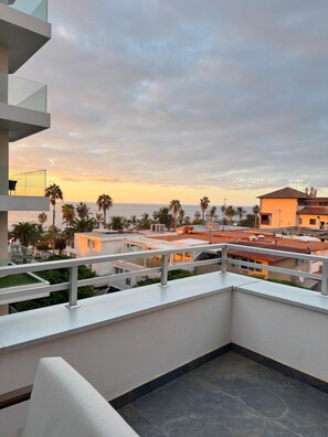 Un balcón con vista al mar y palmeras durante el atardecer.