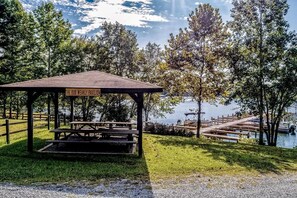 Ein hölzernes Pavillon namens 'The Bob Weakly Pavilion' mit Picknicktischen, umgeben von Bäumen und einem Steg an einem Gewässer.