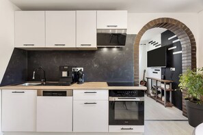 A modern kitchen with white cabinetry, a built-in dishwasher, a coffee machine, and an oven. - Mlinar Wellness Apartment Your Spa Escape (Rečica ob Savinji)