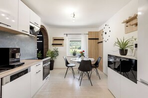 A modern kitchen with a dining area, featuring a built-in oven, a coffee machine, and a dining table with chairs. - Mlinar Wellness Apartment Your Spa Escape (Rečica ob Savinji)