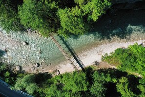 Eine Luftaufnahme eines Flusses mit einer Holzbrücke, umgeben von dichtem Grünwerk.