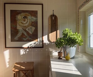 A framed abstract painting, a wooden hanging, a potted plant, a small wooden stool, and a window with natural light. - Sursum: Life slows down at this historic home in Sintra. (Sintra)