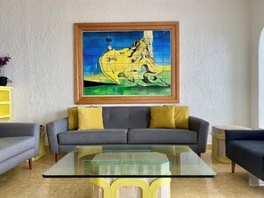 A living room with a sofa, a glass coffee table, and a framed painting on the wall. - Three Bedroom Beachfront Villa - Private Heated Pool & Beach Access (Cancun)