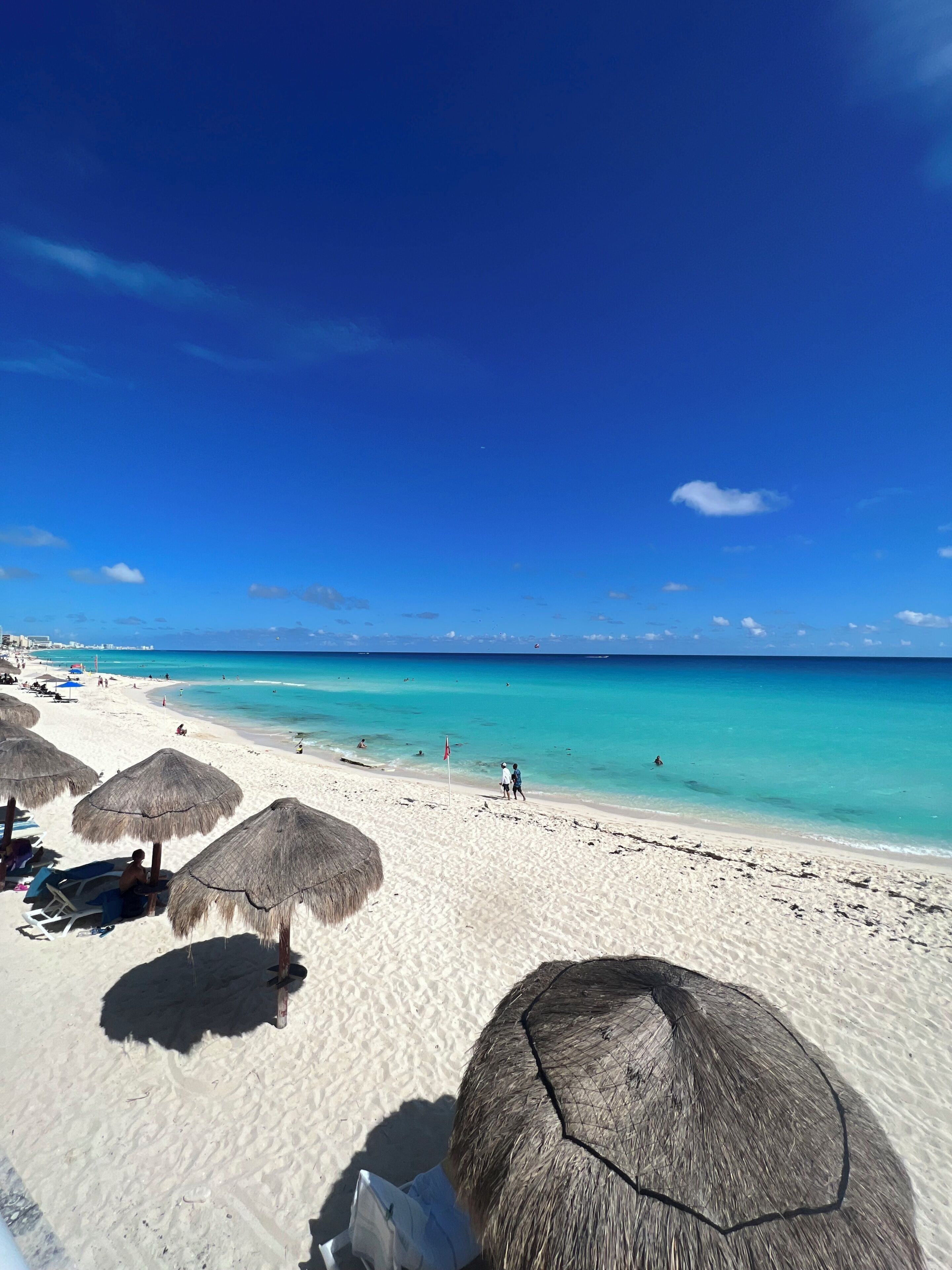 Una playa con arena blanca, agua turquesa cristalina y sombrillas de paja.