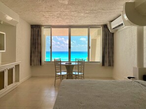 A room with a bed, a table with two chairs, a TV, and a large window with a view of the ocean. - Three Bedroom Beachfront Villa - Private Heated Pool & Beach Access (Cancun)