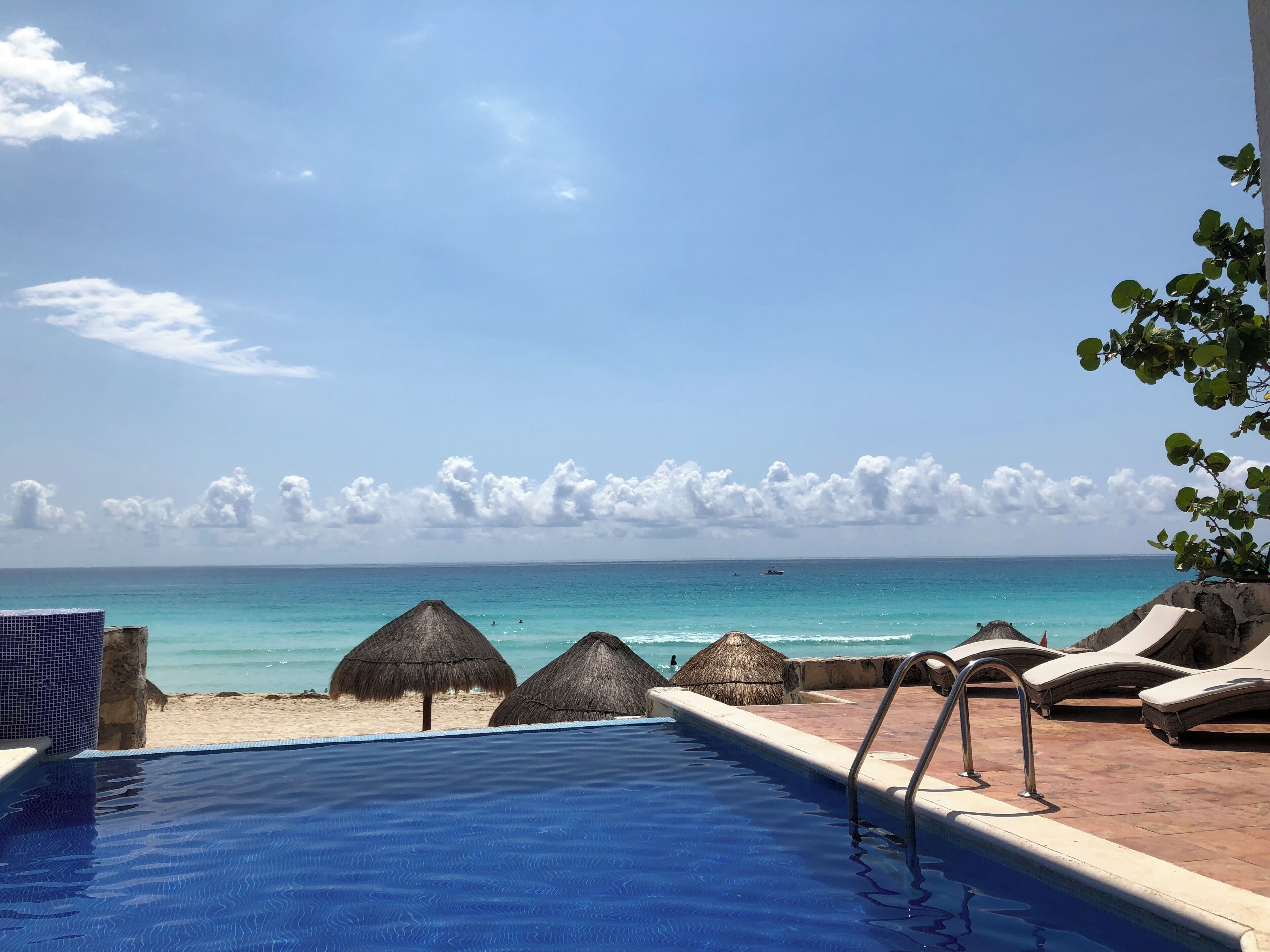 A pool with a view of the beach and ocean, lounge chairs, and thatched umbrellas.