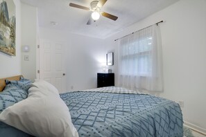 Ein Schlafzimmer mit einem Bett, einem Deckenventilator, einem Schminktisch und einem Fenster mit Vorhängen.
