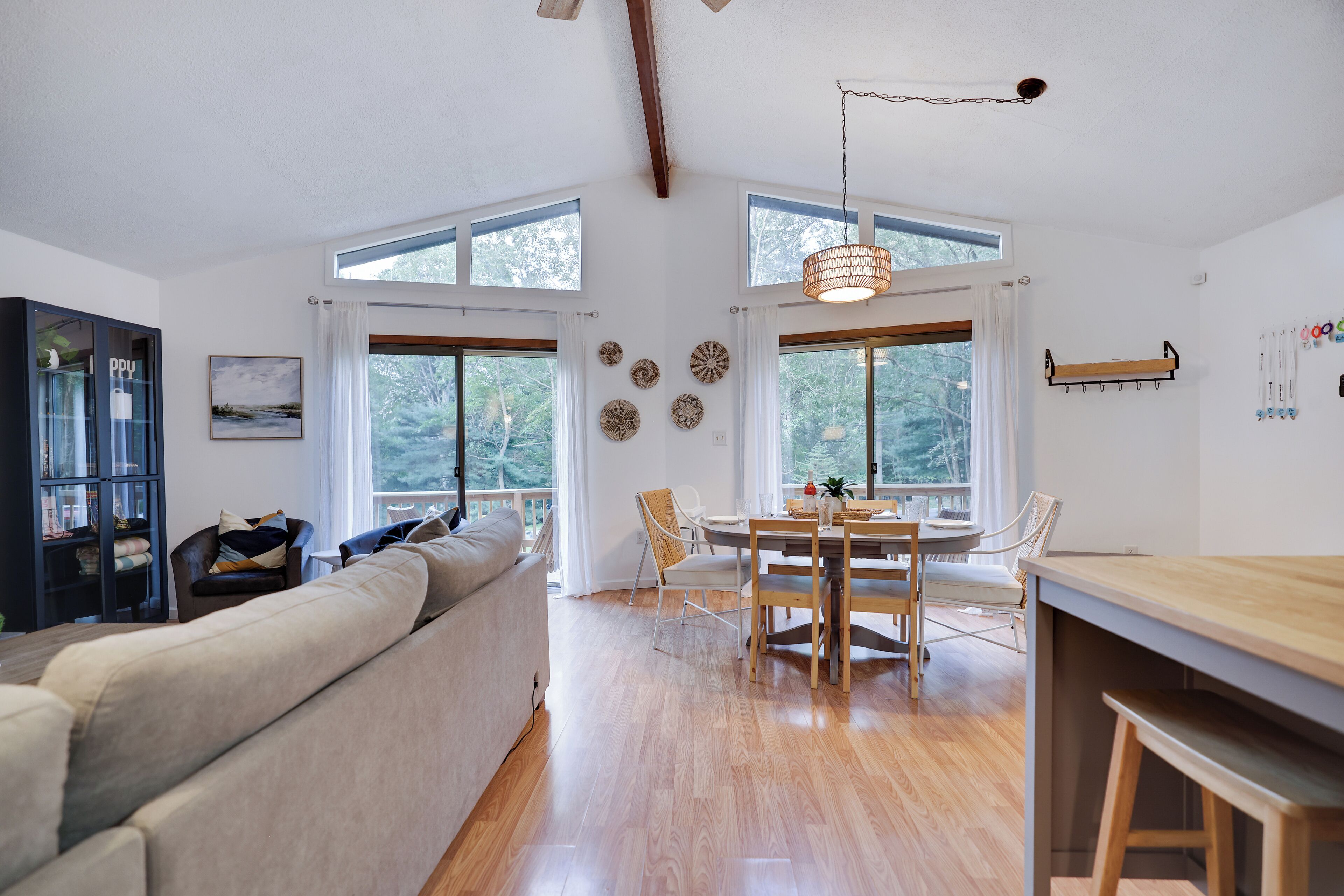A modern living room with a sofa, dining table, and chairs, large windows, and a ceiling fan.