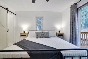 A bedroom with a bed, bedside lamps, a window with blinds, and a view of trees outside. - Pocono Ranch in Bear Creek Lakes - Fire pit, Hammocks, Outdoor Dining (Jim Thorpe)