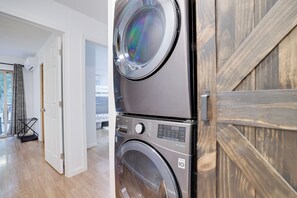 A stacked washer and dryer unit in a modern apartment with a wooden door and a view of the living area. - Pocono Ranch in Bear Creek Lakes - Fire pit, Hammocks, Outdoor Dining (Jim Thorpe)