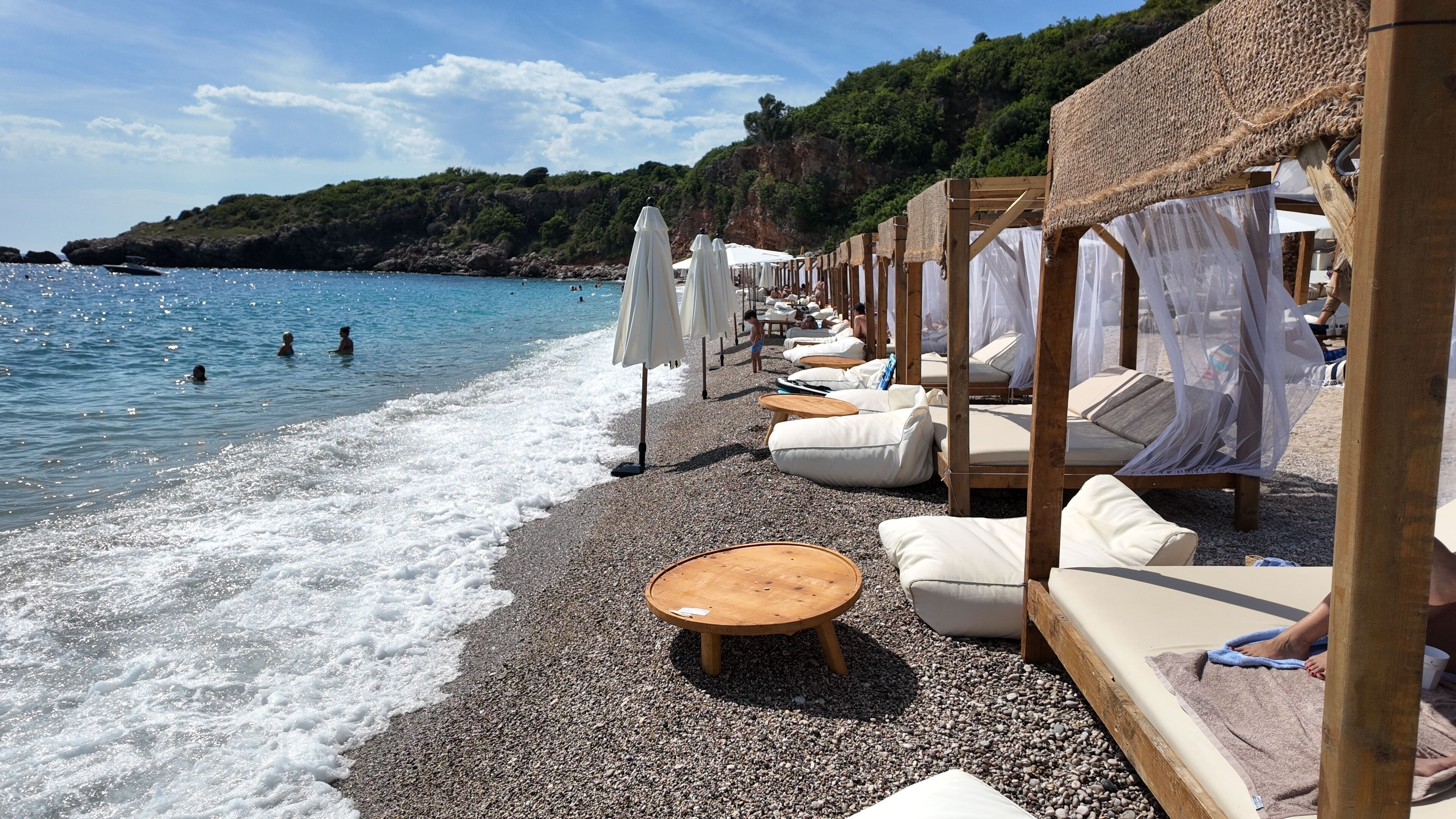 A beachside setting with lounge chairs and umbrellas, a pebble beach, and a view of the sea.