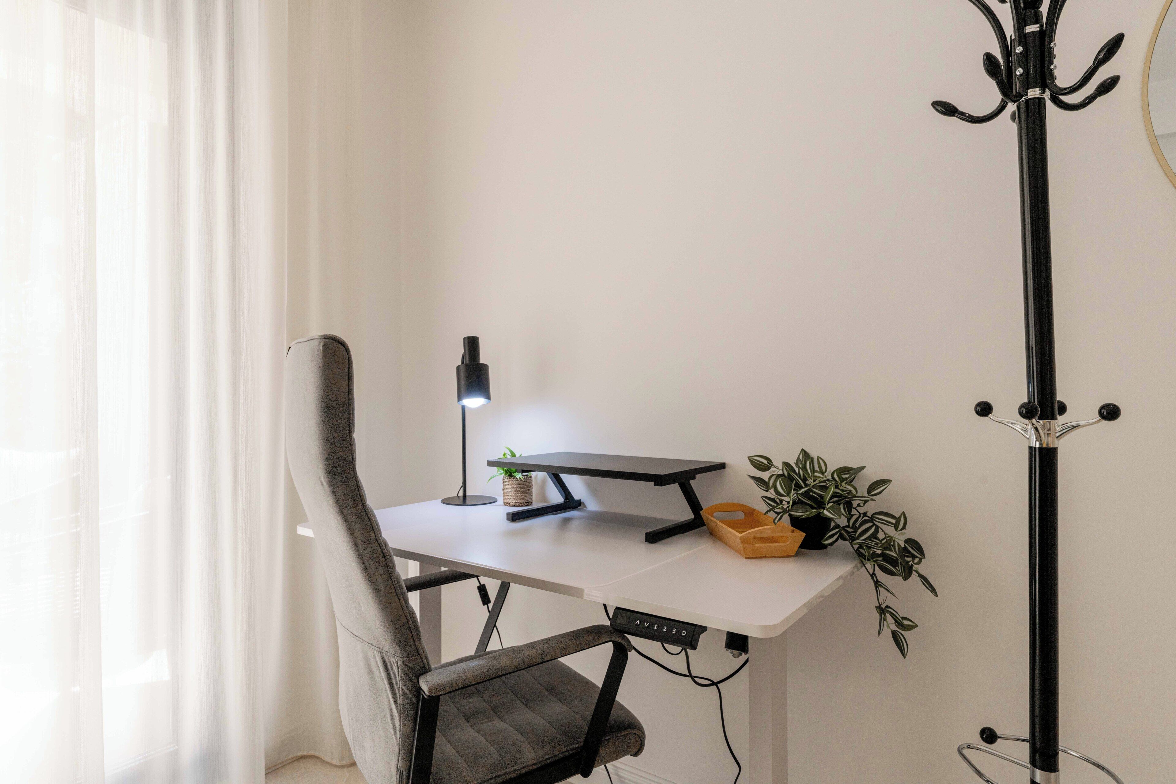 Ein moderner Bürostuhl, ein Schreibtisch mit Lampe, eine kleine Pflanze und ein Kleiderständer.