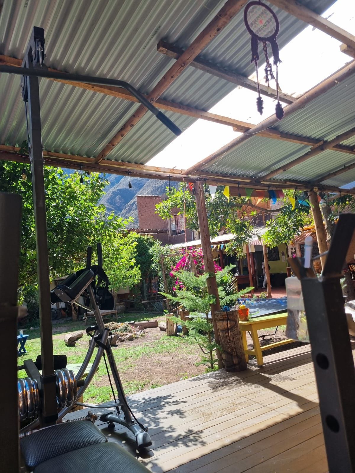 A covered outdoor area with exercise equipment, a wooden deck, and a view of a mountainous landscape.