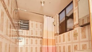 A bathroom with a toilet, a trash bin, a shower curtain, and a mirror. - Kamanti Hostel (Pisac)