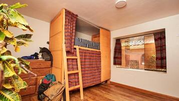 Une petite pièce avec un lit superposé, une armoire en bois et une fenêtre avec des rideaux.