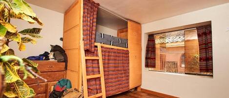 A compact room with a bunk bed, wooden wardrobe, and a window with curtains.
