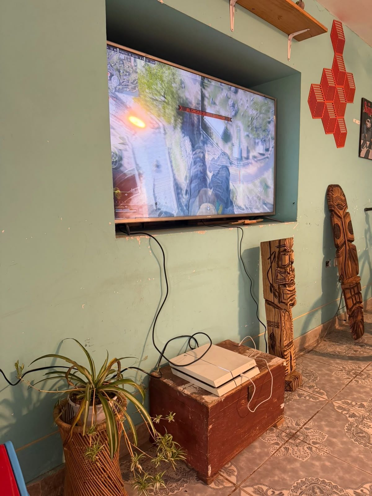 A television mounted on a wall with a game displayed, a wooden chest, and two carved wooden figures.