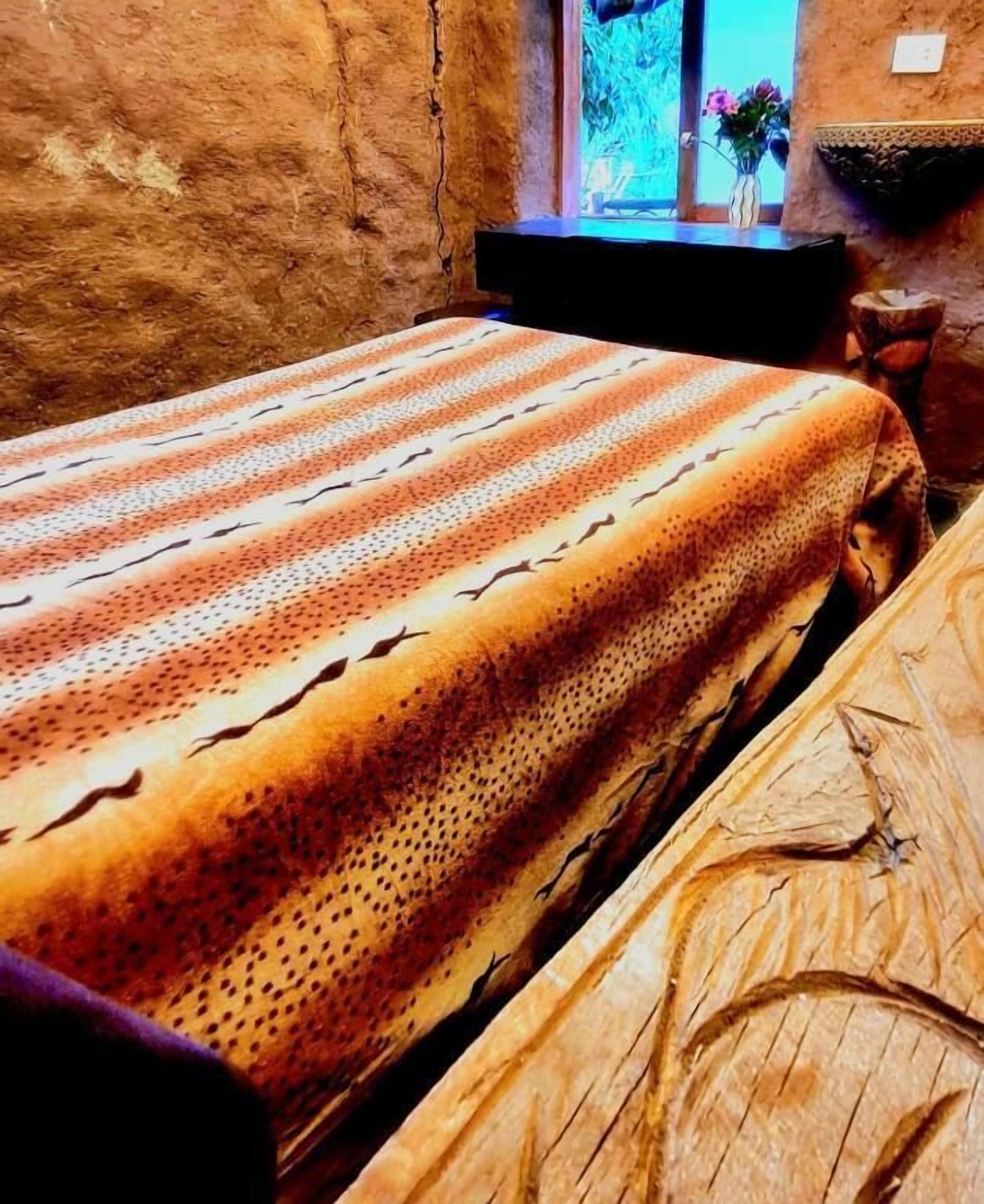 Una cama con colcha estampada, una ventana con vistas y una pared rústica.
