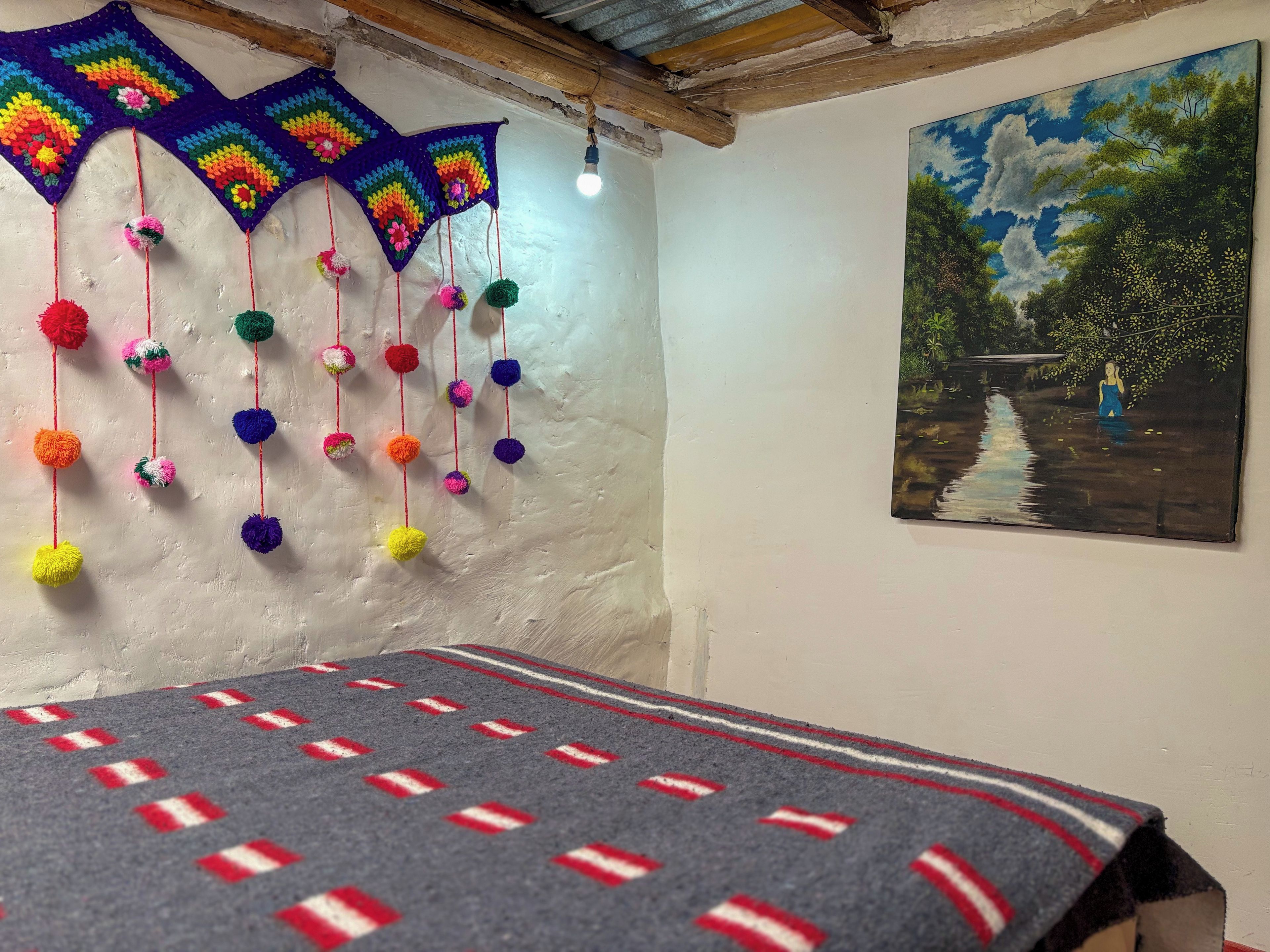 Een kamer met een bed, een kleurrijk gebreide wanddecoratie en een schilderij.