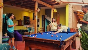 A pool table in a room with yellow walls, wooden beams, and a purple couch. - Kamanti Hostel (Pisac)