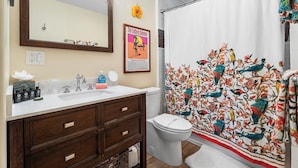 Baño con lavamanos blanco, tocador de madera y cortina de ducha con estampado de pájaros.