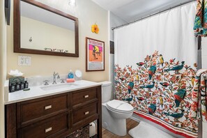 A bathroom with a white sink, wooden vanity, and a shower curtain with a bird pattern. - Kona Shores#223: Top Floor, Split AC, Remodeled! (Kailua-Kona)