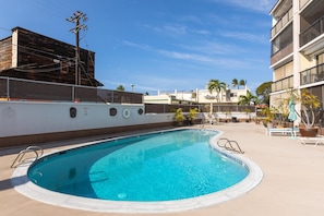 A swimming pool with a clear blue water, surrounded by a concrete deck, and a fence. - Kona Plaza#417: Top Floor, Downtown! (Kailua-Kona)