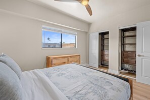A bedroom with a bed, a window, a ceiling fan, and a closet with a mirror. - Kona Plaza#417: Top Floor, Downtown! (Kailua-Kona)