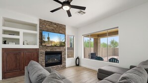 Ein Wohnzimmer mit Kamin, einer Wand aus Stein, einem Deckenventilator und einem großen Fenster mit Blick auf eine Terrasse.