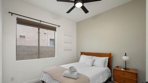 Ein Schlafzimmer mit einem Bett, einem Nachttisch, einer Lampe, einem Deckenventilator und einem Fenster mit Jalousien.