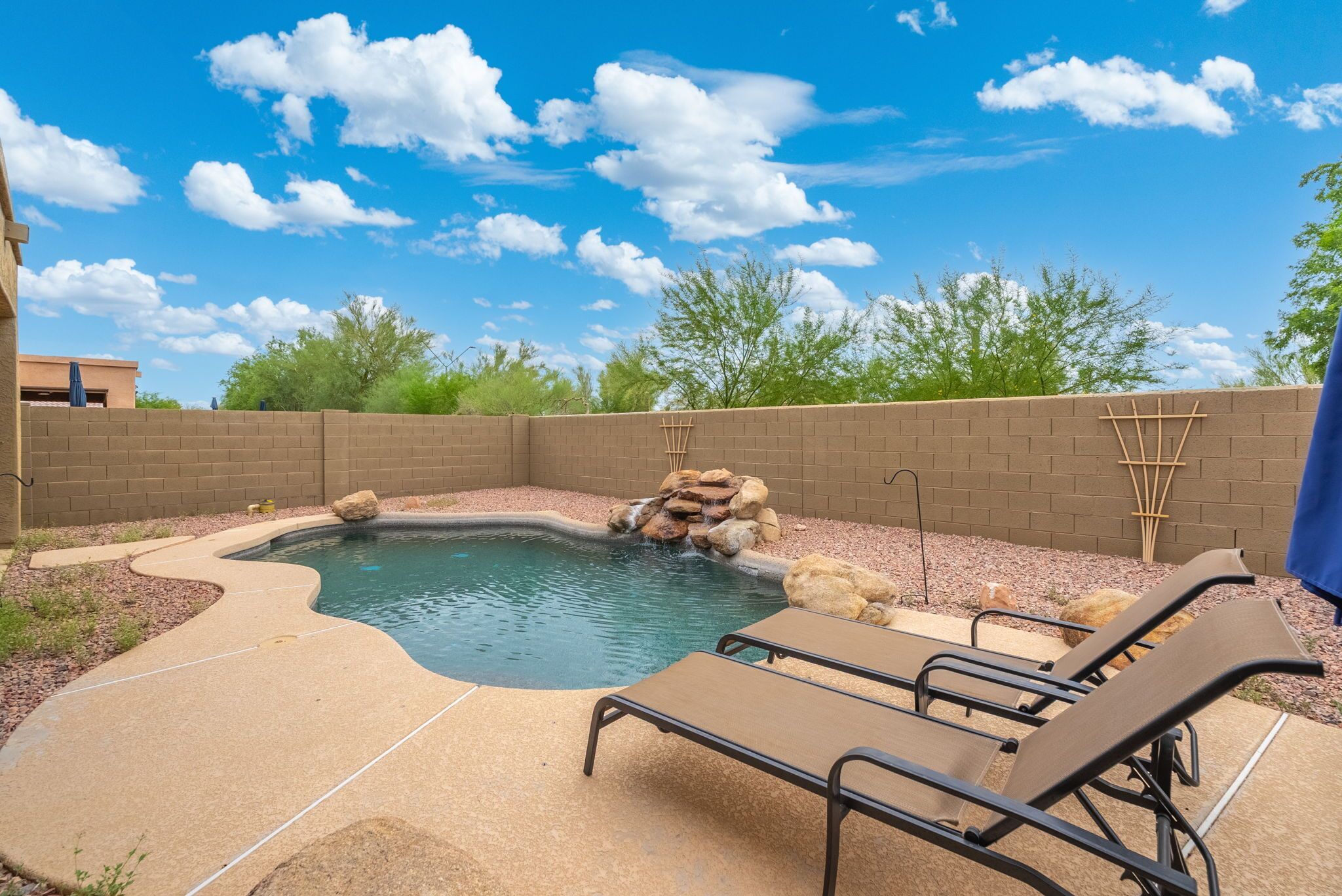 A backyard with a swimming pool, lounge chairs, and a brick wall.