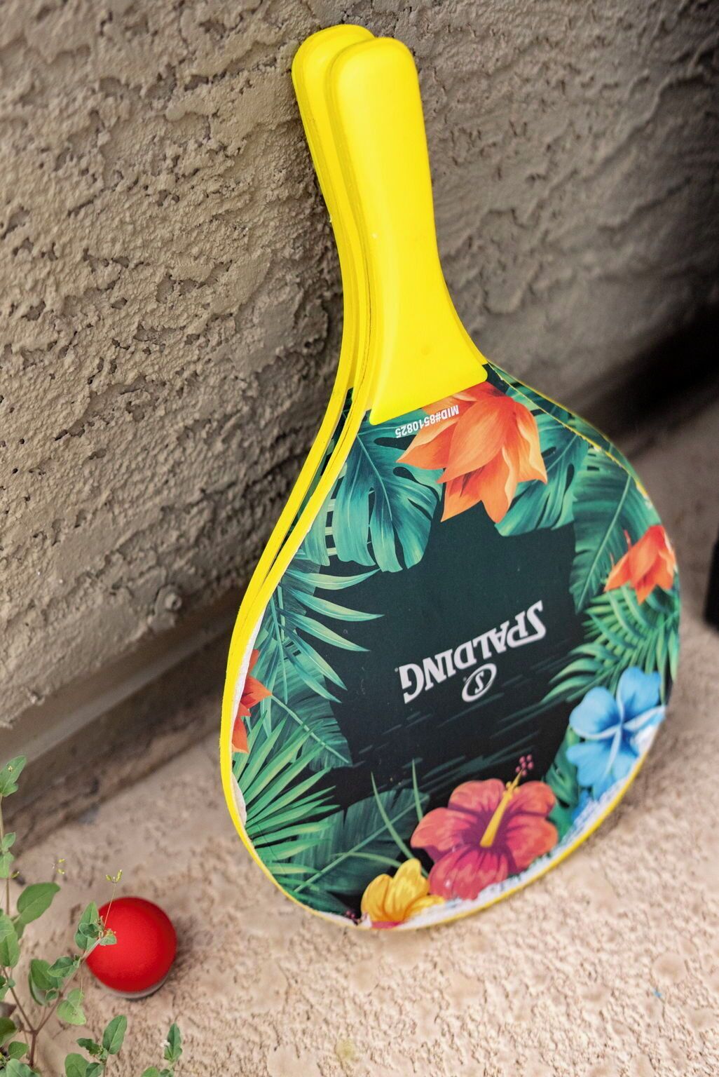 A table tennis paddle with a tropical leaf design, placed on a textured surface.