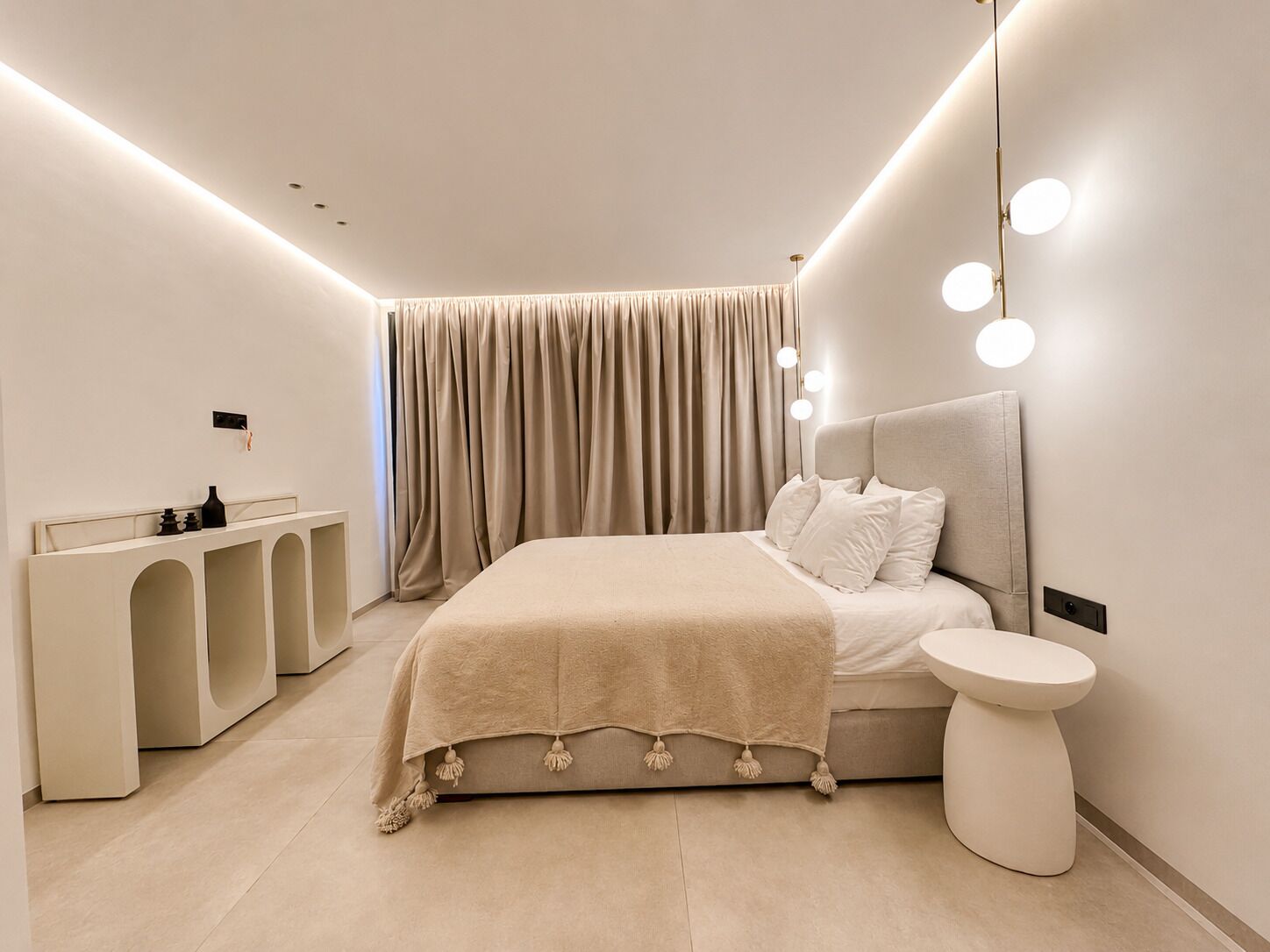 A modern bedroom with a large bed, bedside table, and a vanity with mirrors.