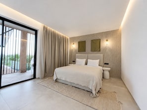 A modern bedroom with a large bed, a sliding glass door leading to a balcony, and two wall-mounted light fixtures. - Architect-designed villa - 5 suites - movie theater & hammam (Marrakech)