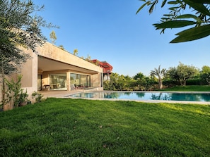 A modern house with a swimming pool, a patio with outdoor furniture, and a well-maintained lawn. - Architect-designed villa - 5 suites - movie theater & hammam (Marrakech)