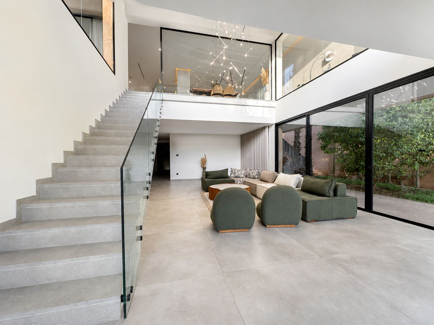 A modern interior with a staircase, a seating area with sofas, and large windows.
