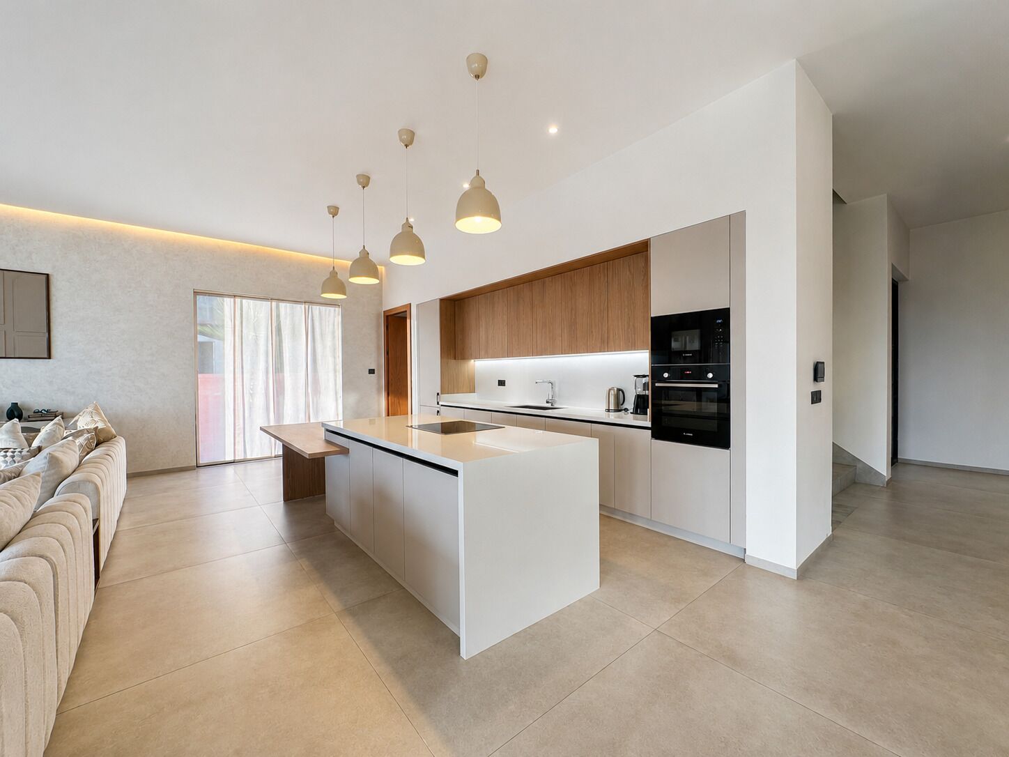 A modern kitchen with a central island, pendant lighting, and a dining area with a sofa.