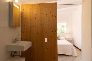 A modern bathroom with a wooden door, a white sink, and a mirror. - Sa Marina by Rentallorca (Son Serra de Marina)