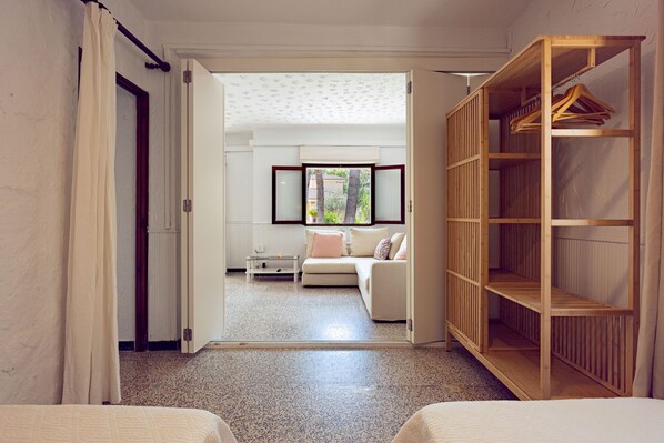 A hotel room with a bed, a seating area with a sofa and a table, a wooden wardrobe, and a view of the outdoors through a window. - Sa Marina by Rentallorca (Son Serra de Marina)