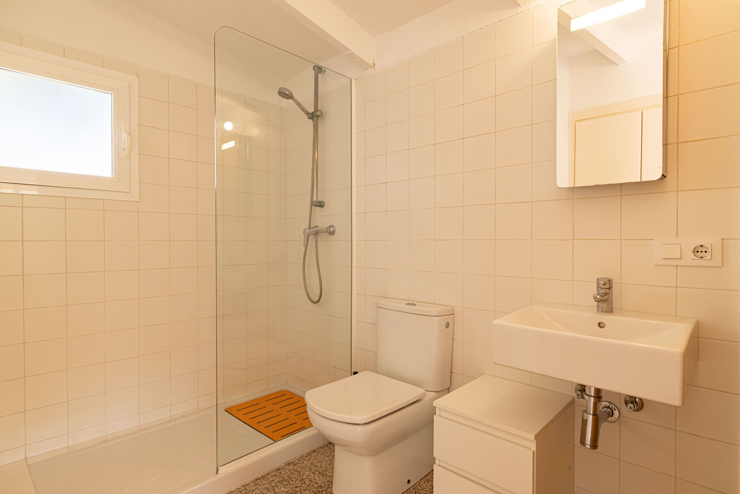 A bathroom with a glass shower enclosure, a white toilet, a sink with a mirror, and a window.