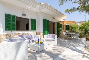 A patio with outdoor furniture, a table with a bowl of fruit, and a view of a building in the background. - Sa Marina by Rentallorca (Son Serra de Marina)