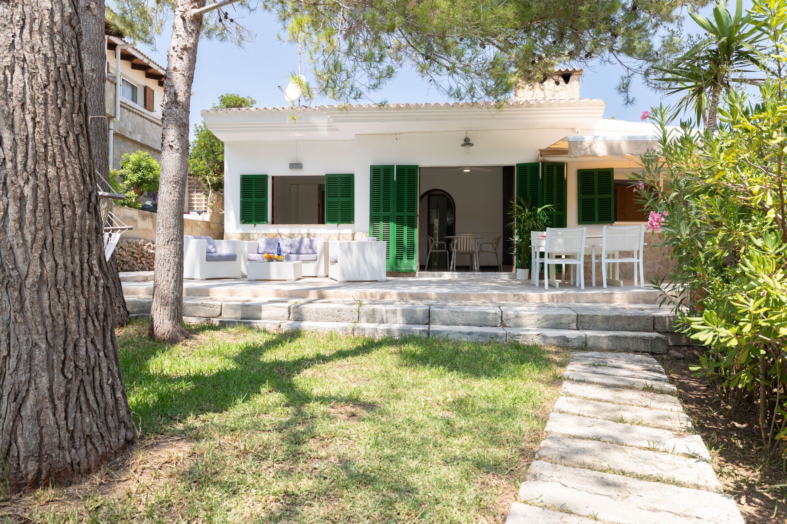 A white building with green shutters, a stone staircase leading to a covered porch, and outdoor furniture.