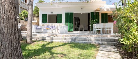A white building with green shutters, a stone staircase leading to a covered porch, and outdoor furniture.
