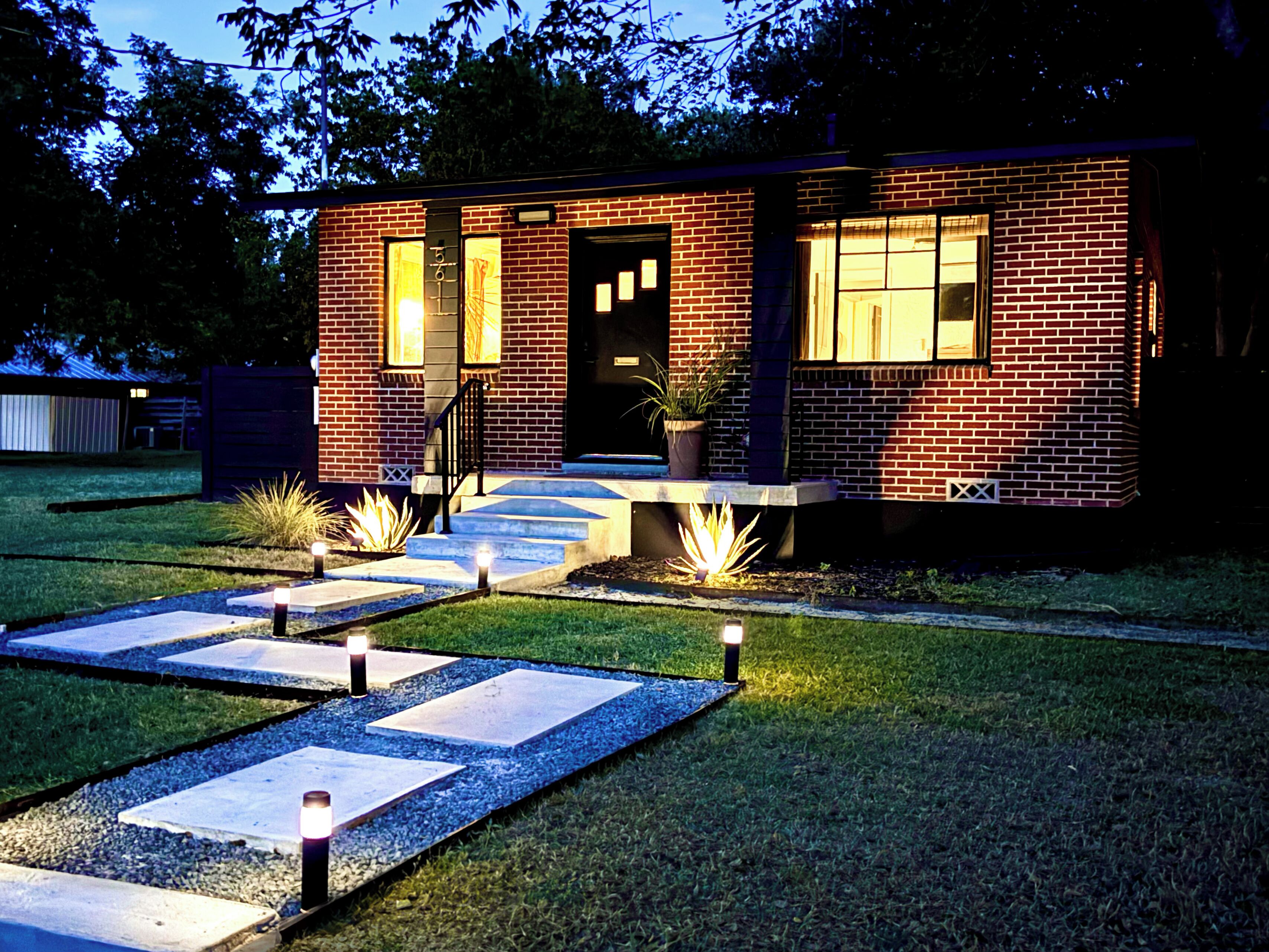 A brick house with a front entrance, a small porch, and a well-lit pathway leading to the door.