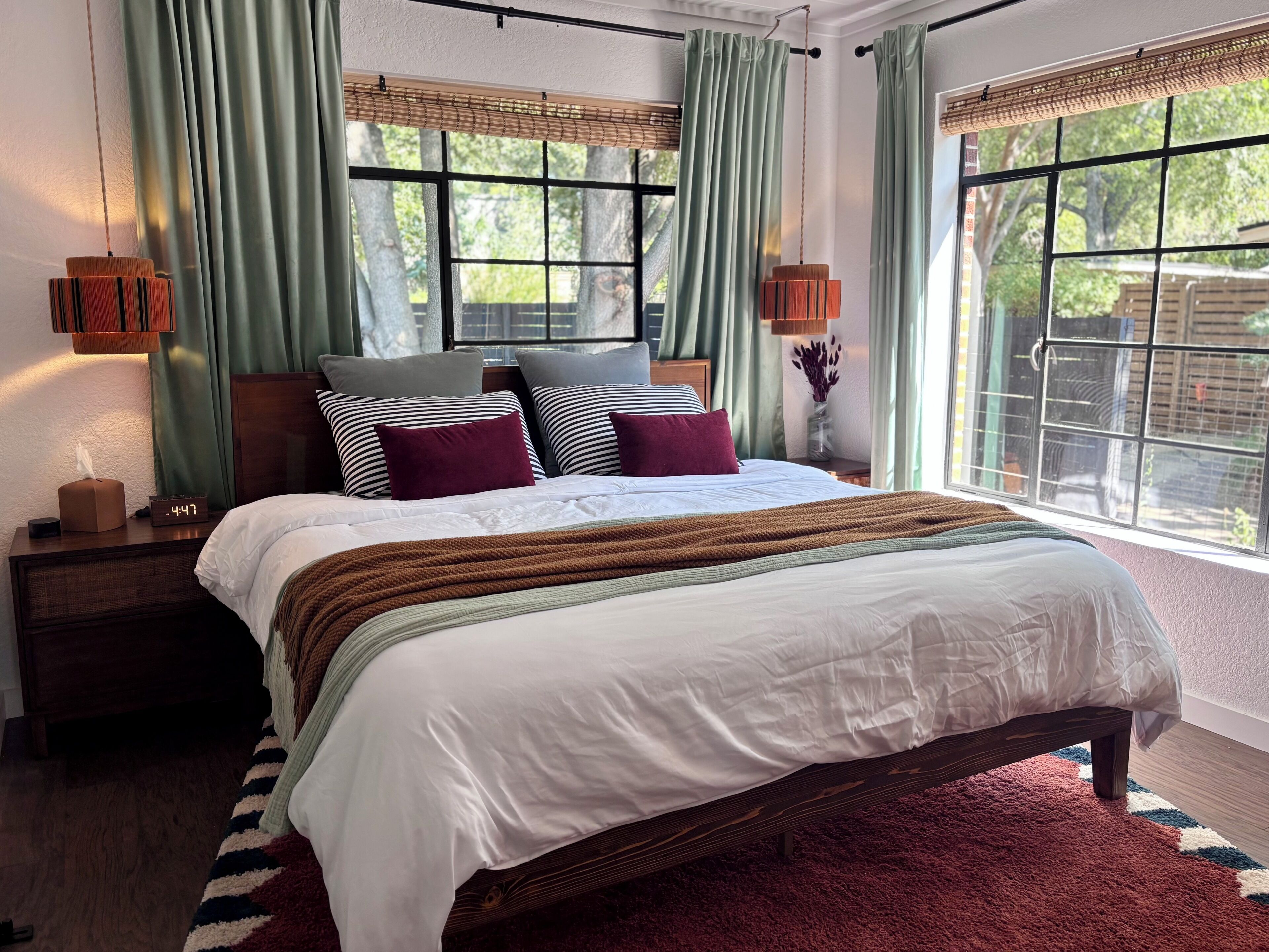A neatly made bed with a white comforter and a brown throw blanket, flanked by pillows in various patterns and colors.