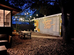 An outdoor seating area with tables and chairs, a wall with a sign, and string lights. - 2 bed 1 bath bungalow in Central Austin. Pet friendly! Minutes to Downtown. (Austin)