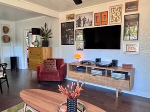A living room with a red armchair, a wooden coffee table, a TV mounted on the wall, and a bookshelf with books and decorative items. - 2 bed 1 bath bungalow in Central Austin. Pet friendly! Minutes to Downtown. (Austin)