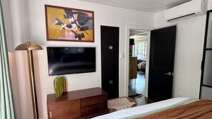 Hotelkamer met een bed, een flatscreen televisie aan de muur, een houten dressoir, een vloerlamp en een schilderij.