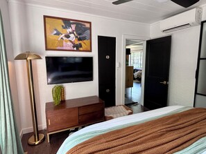 A hotel room with a bed, a flat-screen TV mounted on the wall, a wooden dresser, a floor lamp, and a painting. - 2 bed 1 bath bungalow in Central Austin. Pet friendly! Minutes to Downtown. (Austin)